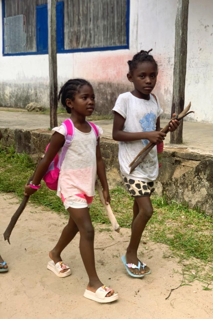 Two girls walking to school carrying a piece of firewood for the canteen