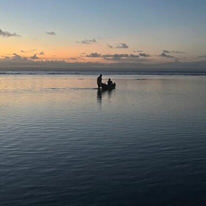 Two people with a pirouge on the sea at dusk