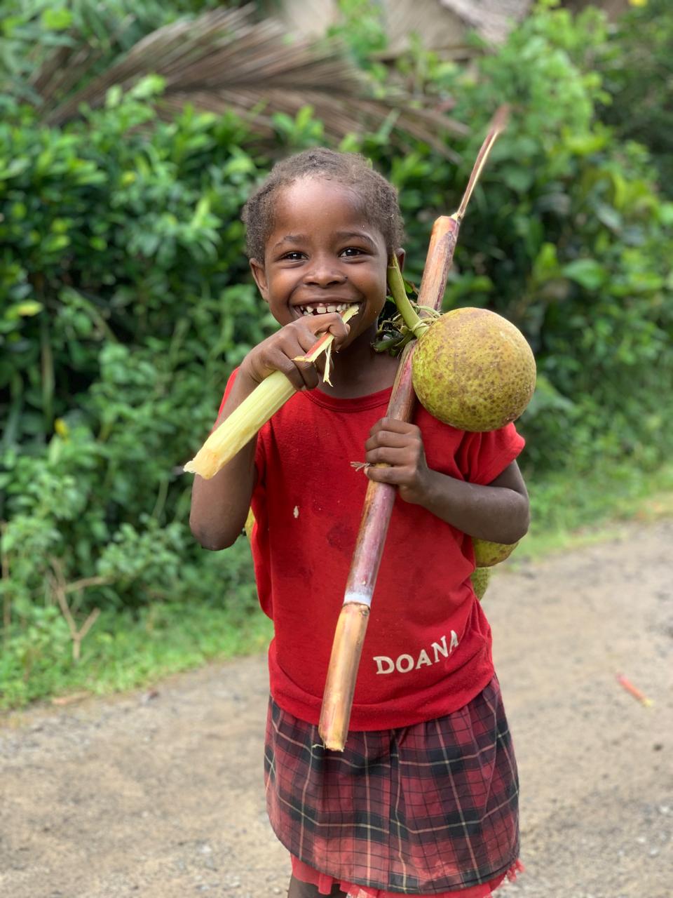 Girl in a village carrying a soanambo fruit and chewing on sugar cane, Madagascar